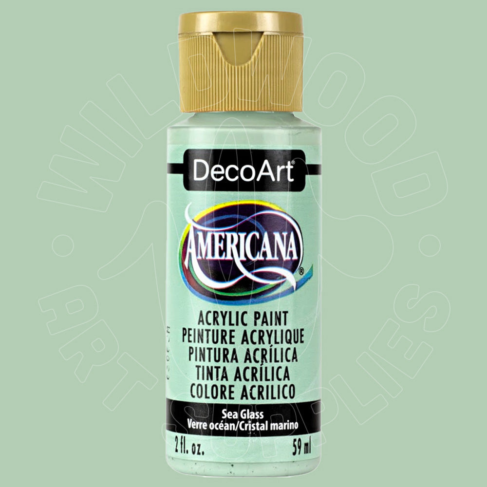 A bottle of DecoArt Americana acrylic paint in the color 'Sea Glass' (Verde ocean/Cristal marino), featuring a light sage green label and a metallic gold cap, set against a matching light sage green background.
