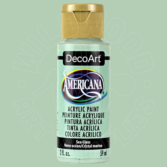 A bottle of DecoArt Americana acrylic paint in the color 'Sea Glass' (Verde ocean/Cristal marino), featuring a light sage green label and a metallic gold cap, set against a matching light sage green background.