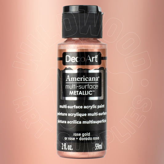 A bottle of DecoArt Americana multi-surface Metallic acrylic paint in the color 'rose gold', shown against a peach-pink gradient background with a faint watermark.