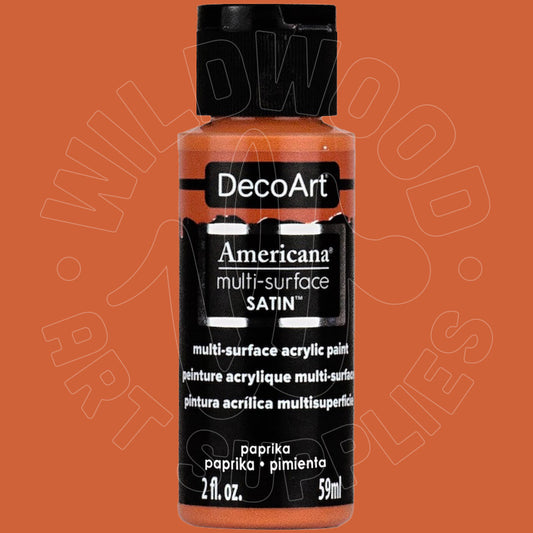 A bottle of DecoArt Americana multi-surface SATIN acrylic paint in paprika, shown against a solid orange background. The bottle has a black cap and a black label with white text, and a faint watermark of 'Wildwood Art Supplies' is visible across the image.